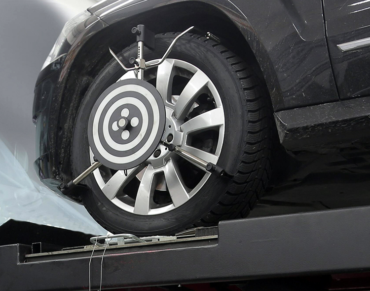 The front left side of an automobile on a lift in a repair shop with tools attached to the tire for a wheel alignment